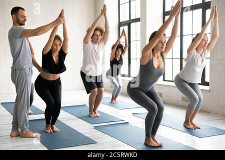 Professional male teacher helping doing chair pose. Stock Photo