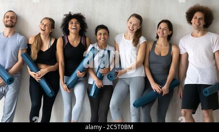 Overjoyed young fit healthy mixed race people holding rubber mats. Stock Photo