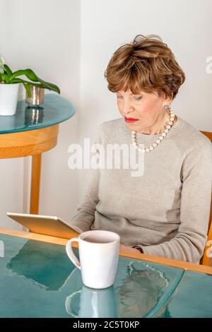 EIghty year old siting woman reading her ipad Stock Photo