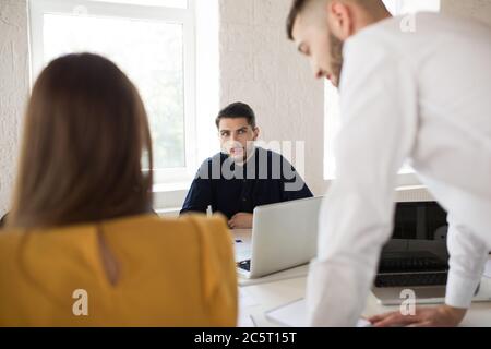 Young businessman in shirt thoughtfully looking aside with laptop. Creative people working together while spending time in modern office Stock Photo