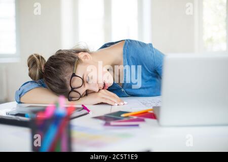 Young tired woman with eyeglasses on head sleeping on desk while working in modern office Stock Photo
