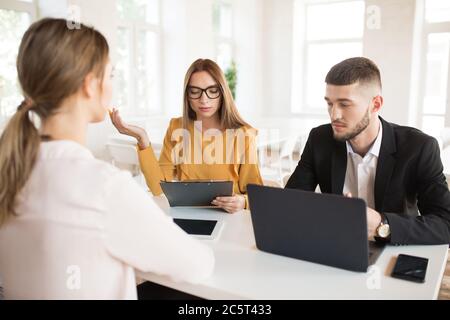 Pensive business man with laptop and business woman in eyeglasses with folder in hand spending job interview in office Stock Photo