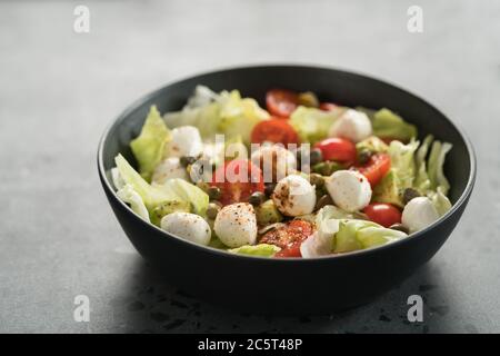 Salad with avocado, tomatoes and mozzarella in black bowl Stock Photo