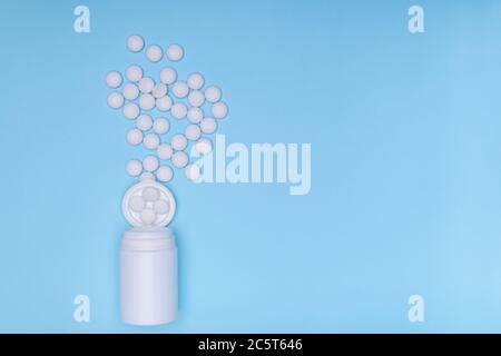 White medicine jar and white pills scattered on pastel blue background. Medicinal and prescription white pills flat background.Copy space Stock Photo