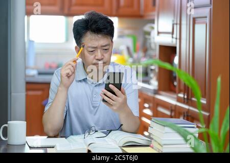 Asian middle-aged man sitting at desk at home, reading a book and studying. Stock Photo
