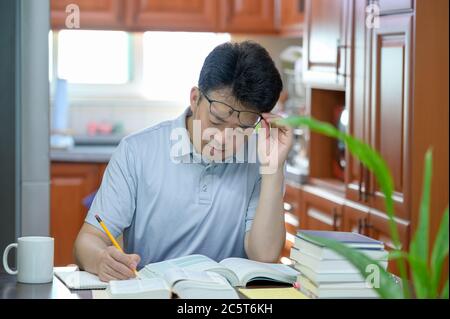 Asian middle-aged man sitting at desk at home, reading a book and studying. Stock Photo