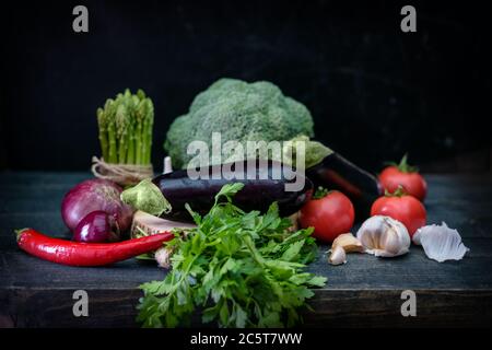 Beautiful still life with a low key. Unusual light from the window on raw and fresh vegetables lying in a pile on the shelf. Stock Photo