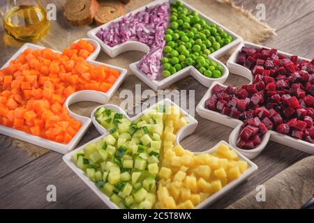 Raw vegetables carrots, peas, onions, cucumber, potatoes, beets cut into cubes lie on plates that are collected in puzzles. Stock Photo