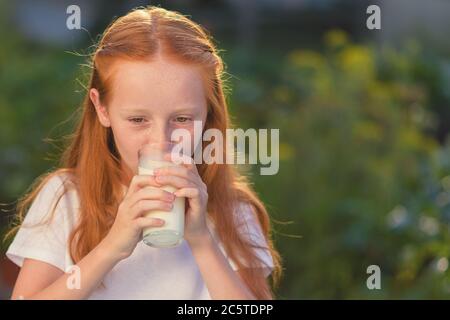 Milk is fresh from the cow - beautiful girl with dairy products. Healthy baby milk - Portrait beautiful redhead girl drinking fresh milk outdoors. Stock Photo
