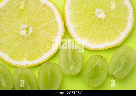 A slices of lemon and berries of white grapes on a background of light green color. Summer bright wallpaper, pattern. Green and yellow color texture Stock Photo