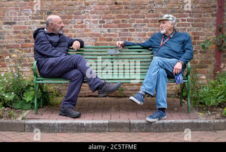 London UK. June 2020. Two retired men sitting at either ends of a park bench having a socially distanced conversation during the Coronavirus lockdown. Stock Photo