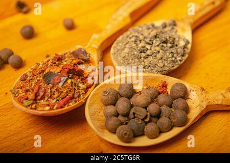 Black allspice, coarse salt and various ground spices in wooden spoons on a wooden Board. Close up Stock Photo