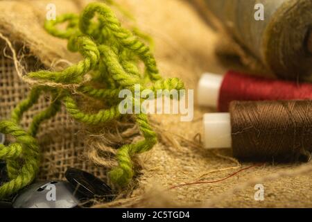 Various buttons and multicolored threads on coarse-textured burlap. Close up Stock Photo