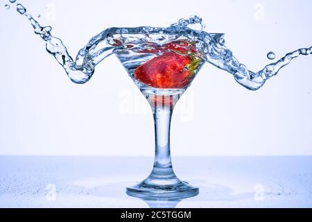 Frozen splashes of clean, spring water, in a glass with frozen strawberries, on a white background. Stock Photo