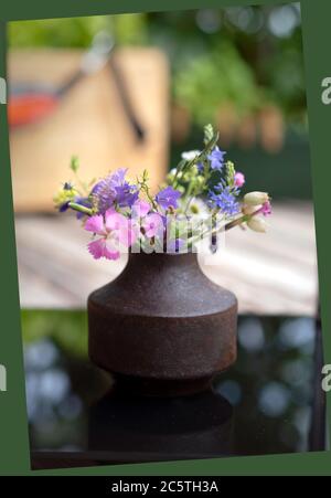 Mini bouquet of Alps mountains on glass surface, outside. Pink and purple field flowers in a vintage brown vase Stock Photo