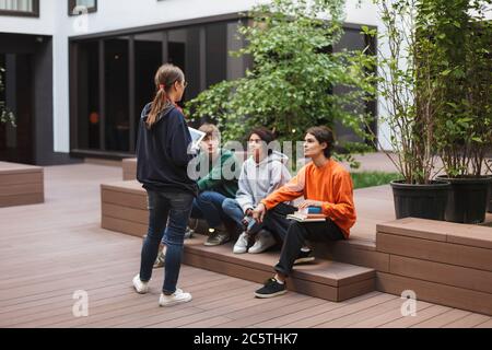 Group of cool students sitting and preparing for lesson while studying together in courtyard of university Stock Photo