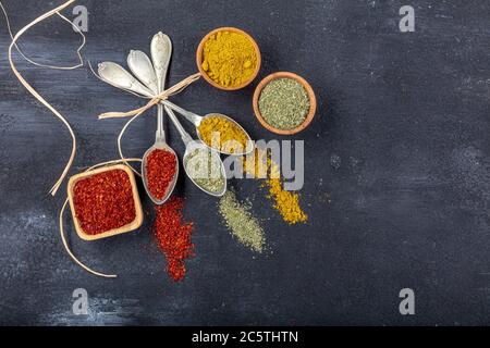 Top view of different kinds of colorful spices in spoons on black stone surface. Creative food concept texture with blank copy space for your message Stock Photo