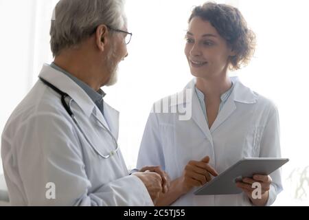 Smiling diverse doctors talk discuss issue using tablet Stock Photo