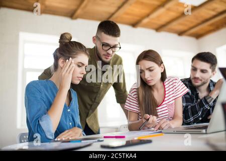 Group of pensive men and women thoughtfully working with sketches while spending time at work. Young creative people thinking about new project Stock Photo
