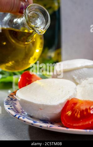 Making of fresh caprese salad with soft Italian cheese from Campania buffalo mozzarella with ripe tomatoes, basil and olive oil close up Stock Photo