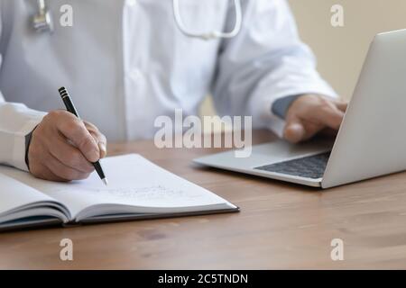 Close up of male doctor work on computer making notes Stock Photo