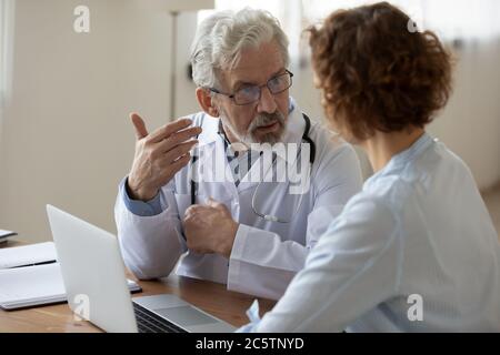 Senior male doctor consult female patient using laptop Stock Photo