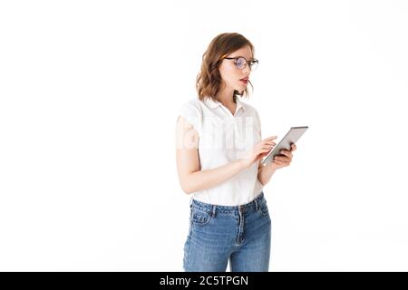 Portrait of beautiful lady in eyeglasses standing and thoughtfully working on the tablet on white background isolated Stock Photo
