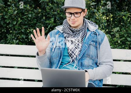 A Caucasian man sits on a bench and communicates via video chat on a laptop Stock Photo
