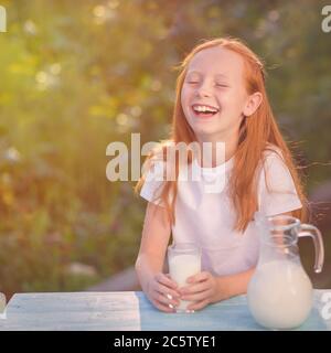 Milk is fresh from the cow - beautiful girl with dairy products. Healthy baby milk - Portrait  beautiful redhead girl drinking fresh milk outdoors. Stock Photo