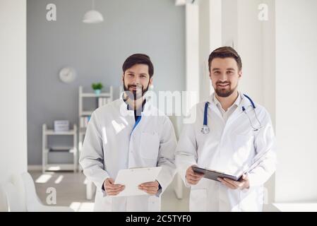 Two practicing doctors with clipboard standing in a clinic office. Stock Photo