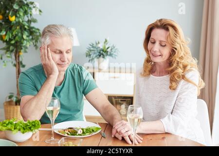 Portrait of loving mature couple holding hands while enjoying romantic dinner at home, copy space Stock Photo