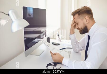 Serious busy businessman thinks working documents sitting at a table with a computer in the office. Stock Photo