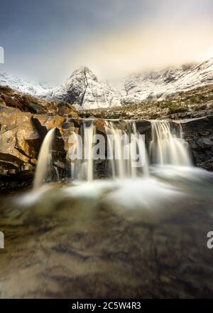 Fairy Pools Waterfall On The Isle of Skye With Snowcapped Mountains. Stock Photo
