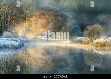 Peaceful misty morning in the English Lake District National Park with Autumn colours reflecting in still calm river. Stock Photo