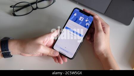 CHIANG MAI ,THAILAND - JULY 3, 2020 : Woman hand holding iPhone X to use facebook with new login screen.Facebook is a largest social network and most Stock Photo