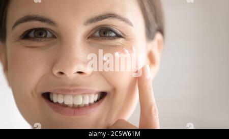 Close up smiling beautiful woman applying moisturizing face cream Stock Photo