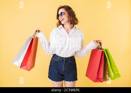 Portrait of beautiful smiling lady in sunglasses standing with colorful shopping bags in hands on over pink background Stock Photo