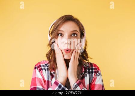 Portrait of pretty girl in colorful shirt standing in headphones and amazedly looking in camera on over pink background Stock Photo