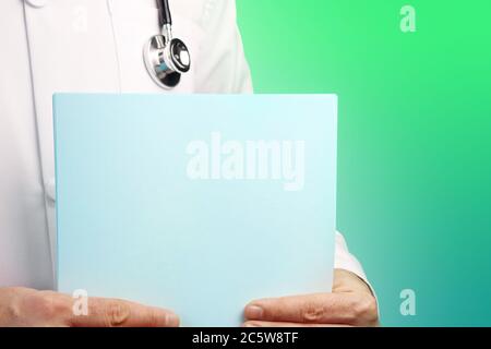 Male Doctor with stethoscope holds medical report in his hands. Cutout. Green turquoise background. Healthcare, Medicine. Mockup Stock Photo