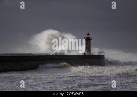 Big white waves over piers and lighthouse against a stormy dark cloudy sky. Douro river mouth, Porto, Portugal. Stock Photo