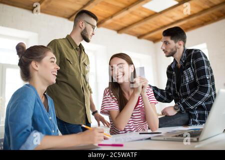 Two cheerful girls happily laughing while spending time in modern office with colleagues on background. Group of creative people working together Stock Photo
