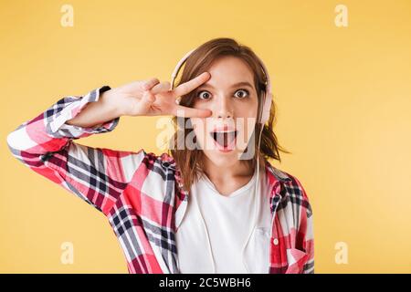 Portrait of cool girl in colorful shirt standing in headphones and amazedly looking in camera on over pink background Stock Photo