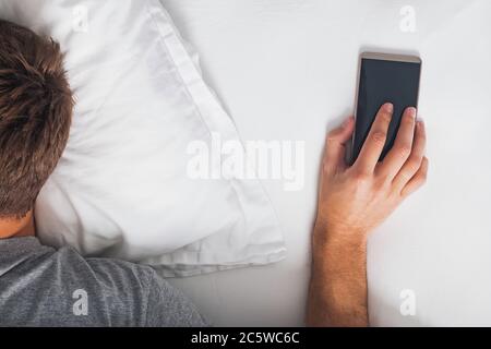 Close-up of man holding hand on phone at the morning, snoozing the alarm Stock Photo