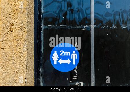 Blue sign taped on a wall outside a shop reminding compliance with 2m social distancing during the Covid-19 pandemic emergency Stock Photo