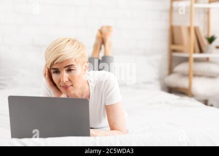 Successful woman lying on bed working on laptop Stock Photo