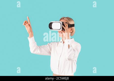Female entrepreneur in virtual reality headset pushing button on virtual screen on blue background Stock Photo