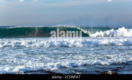 Ocean wave upright wall of blue and white water crashing on shallow reef sandbars . Stock Photo