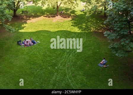 Two groups of people sitting on the grass in the park. The first group is having a picnic, the second is meditating. Stock Photo