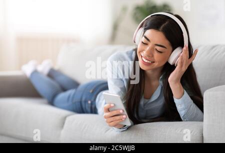 Music App. Positive Girl In Headphones, Listening Songs On Smartphone At Home Stock Photo