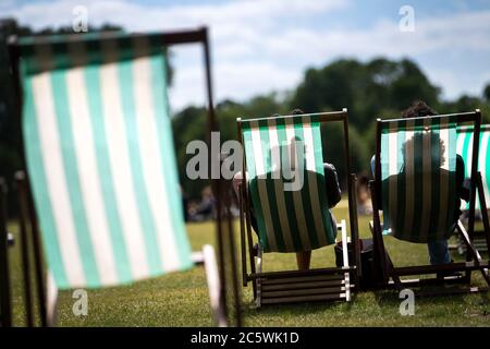 People sit in deck chairs enjoying the warm weather in Hyde Park, London as the chairs are brought out for the first time since the coronavirus crisis. Stock Photo